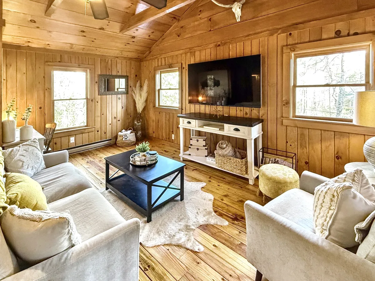 A living room with comfortable sofas, a coffee table, and large windows that offer views of the outdoors. The space is arranged for socializing and relaxing, with warm, inviting decor that suggests cozy gatherings, game nights, and movie marathons while being visually connected to the outside world through the windows.