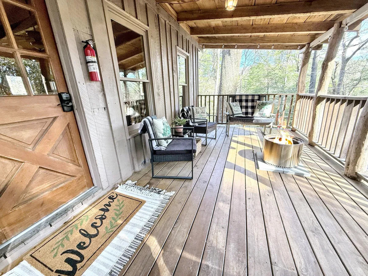 An inviting wooden deck with comfortable seating surrounds a fire pit, with a welcome mat at the entry. The setting is perfect for stargazing, fireside gatherings, and enjoying the peaceful ambiance of the surrounding nature.