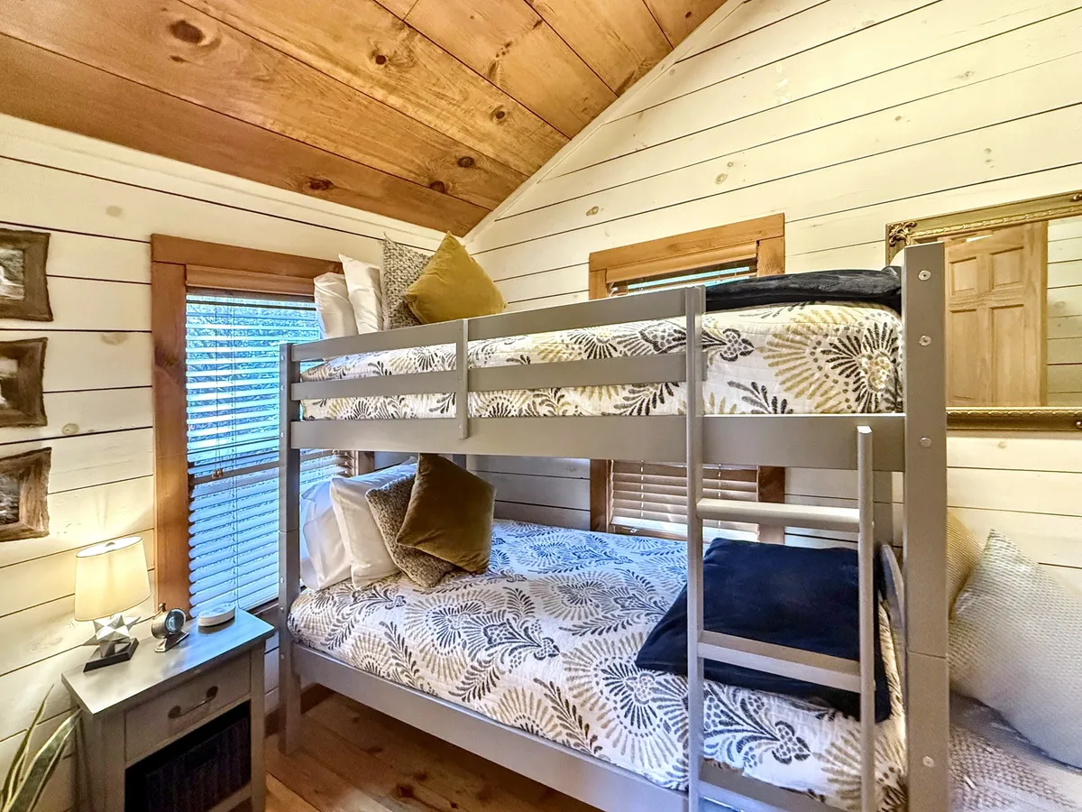 A cheerful bunk room with sturdy wooden bunk beds, decorative pillows, a table lamp, and framed artwork on the walls. The wooden surfaces and playful decor create a welcoming atmosphere ideal for families or nostalgic adults seeking a touch of the past.
