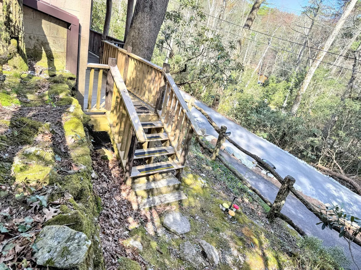 A tranquil scene of wooden steps leading from a cozy porch into moss-covered rocks and dense natural surroundings. The lush greenery creates an inviting atmosphere, suggesting easy access to hiking trails and the serenity of the woods just outside the cabin.