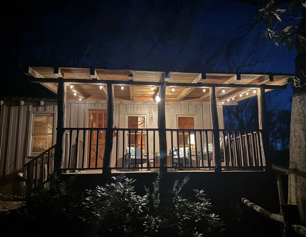 A cozy wooden deck adorned with string lights and comfortable outdoor seating. The setting is perfect for evening gatherings, quiet relaxation under the stars, or enjoying a warm drink while listening to the sounds of nature.