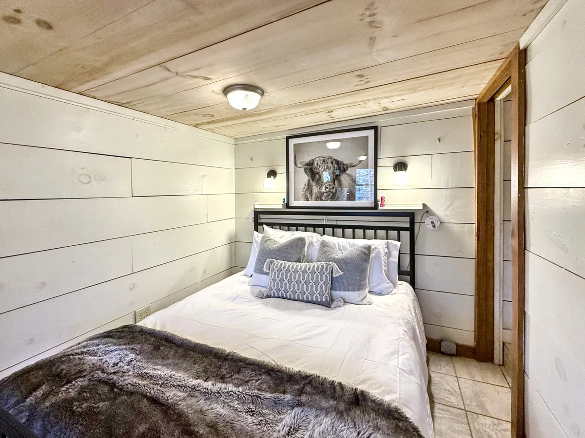 A serene master bedroom with a plush bed framed by elegant wall sconces and calming, framed artwork. Natural light softly enters the space, highlighting its inviting and peaceful ambiance—perfect for restful nights or morning relaxation.