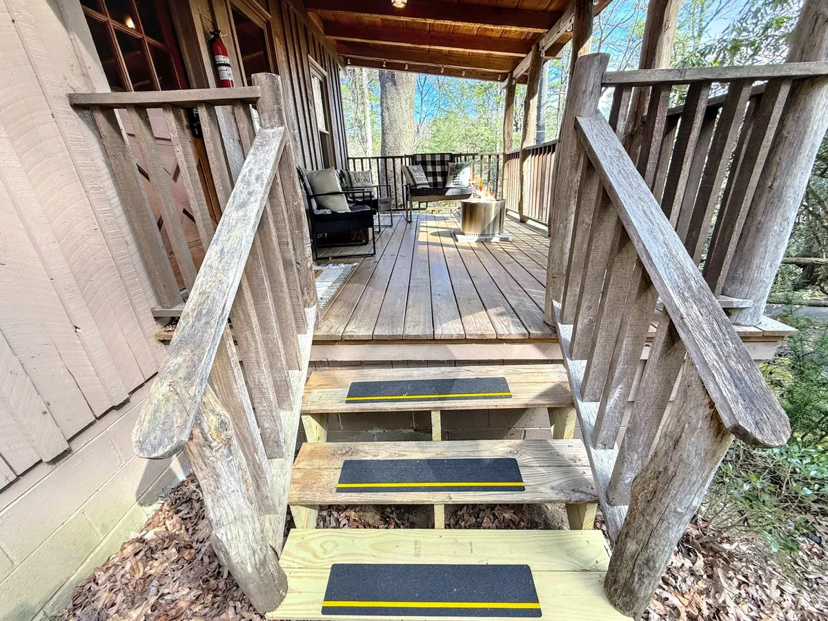 A cozy exterior seating area sits atop wooden stairs, bordered by a railing and shaded by surrounding trees. The setup is ideal for relaxing with coffee or enjoying social moments, echoing the leisurely experiences found in downtown cafés and gathering spots.