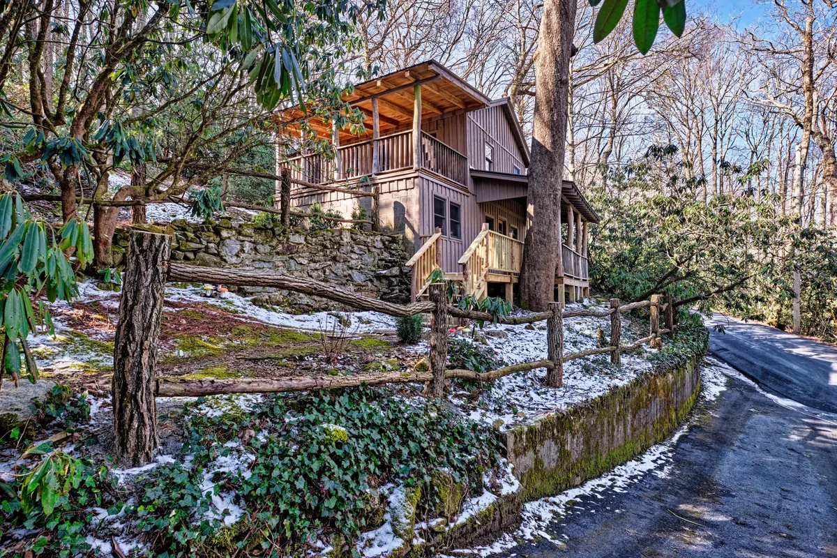 This image captures the wooden porch of the cabin, framed by a stone wall, lush surrounding greenery, and a welcoming path leading up to the house. The scene suggests a tranquil setting perfect for beginning or ending a day of exploring nearby attractions.